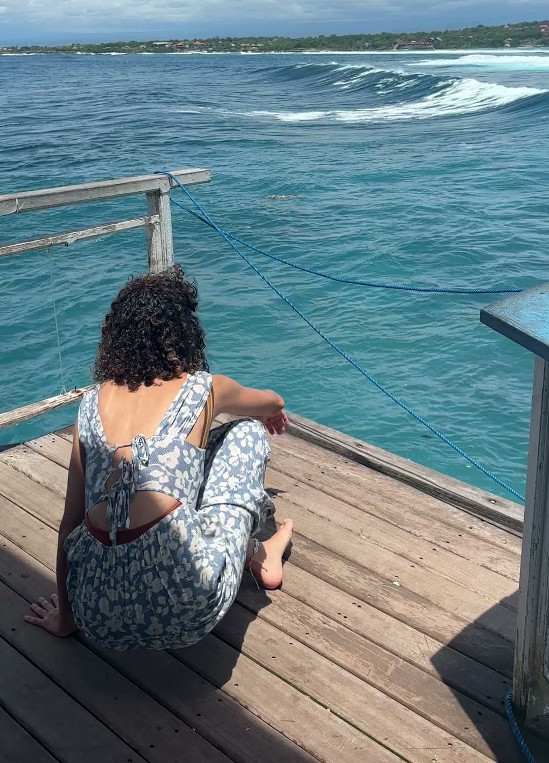 Melis sitting on a wooden pier, looking out at the waves